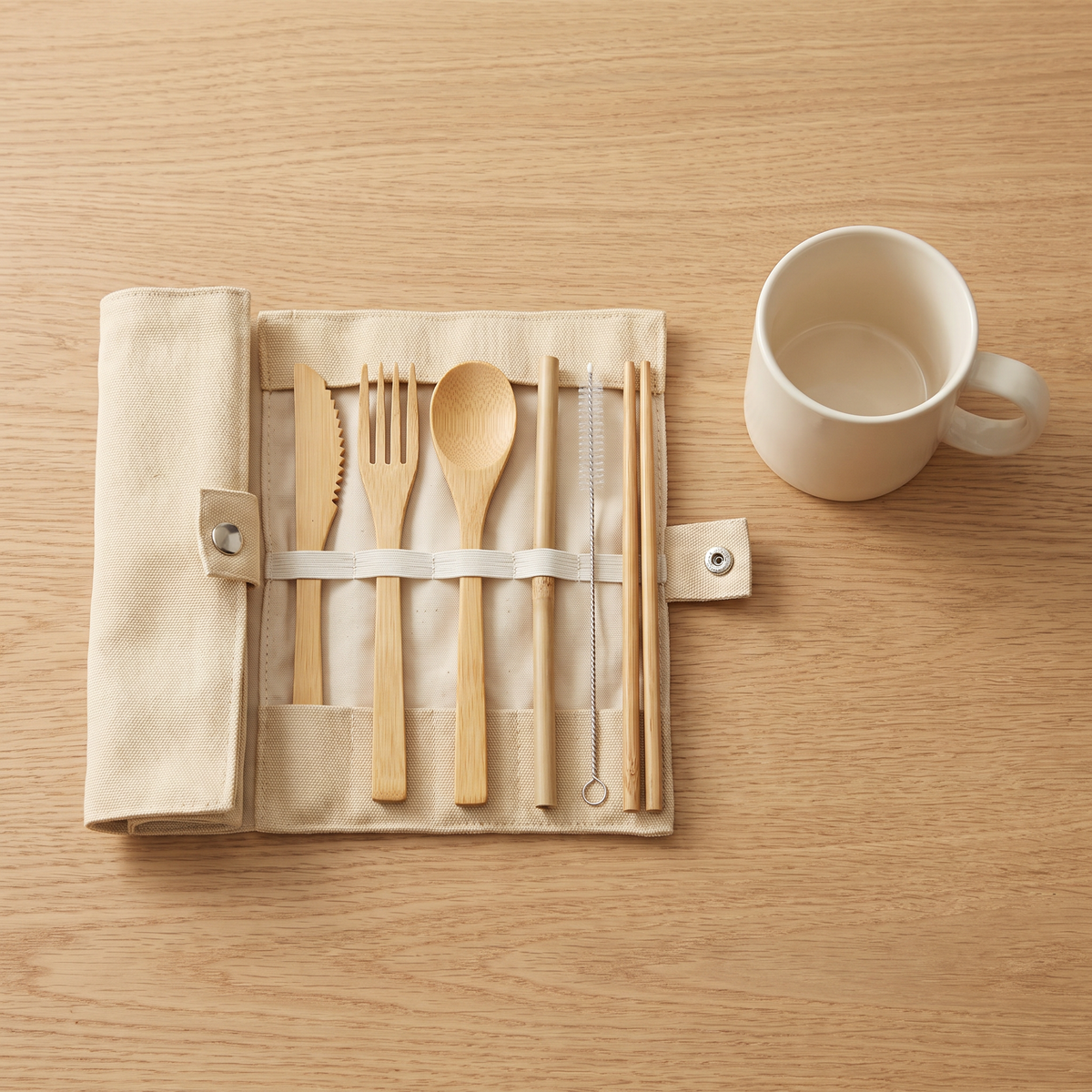 The open pouch with every bamboo piece in place, next to a cream mug for size