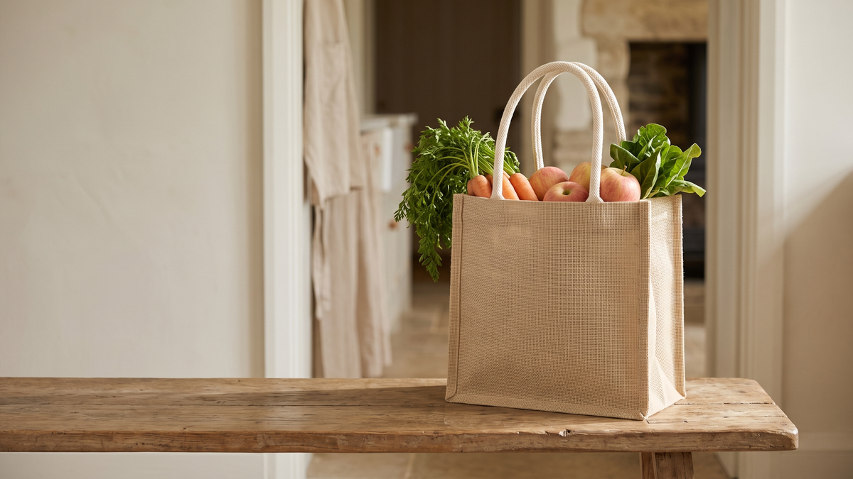 Woven tote filled with carrots and greens on a wooden bench in a hallway
