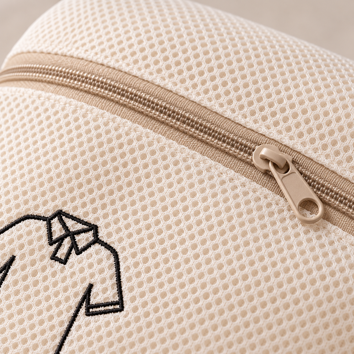 Close-up of fine cream mesh, tan zip pull and an embroidered shirt icon