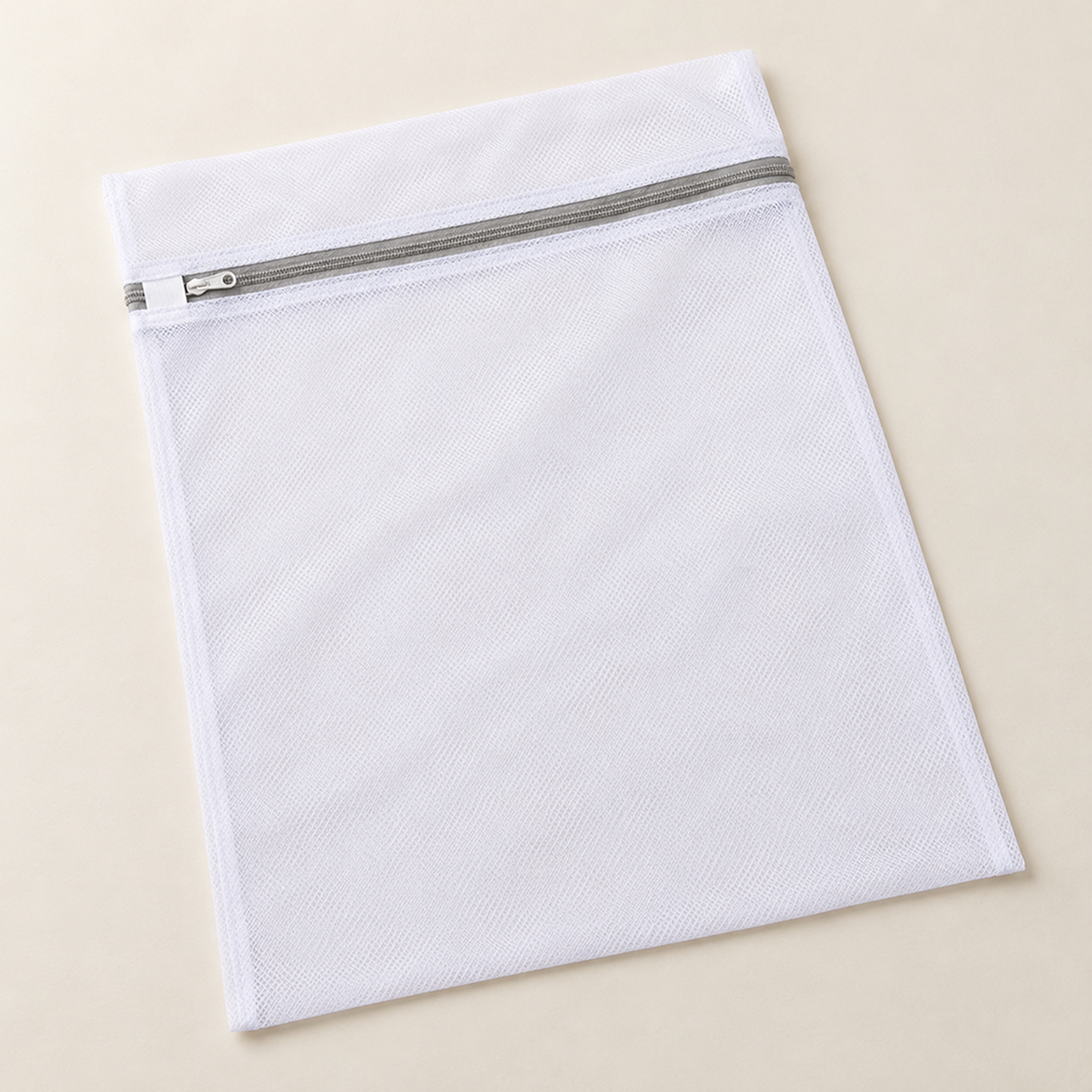 Empty flat white mesh bag laid on a pale surface, zip across the top