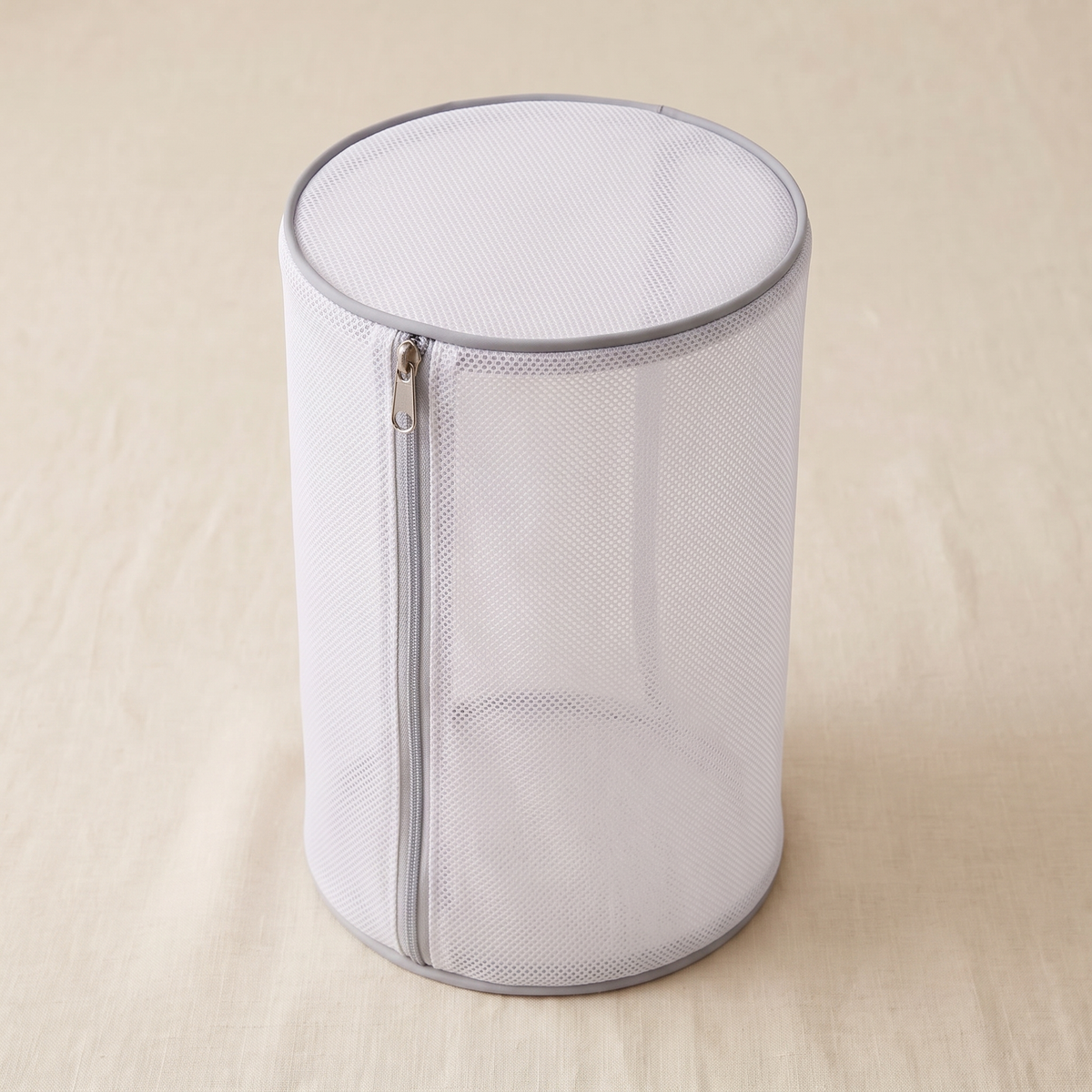 Upright cylindrical mesh bag with grey trim on a pale fabric surface