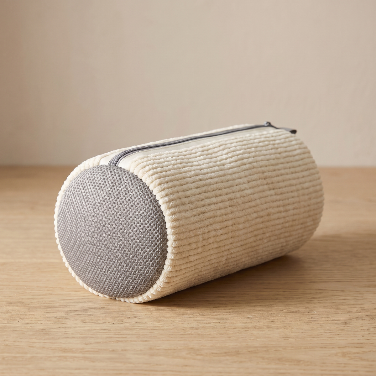 Cream cylindrical wash bag with a grey mesh end on a wooden surface