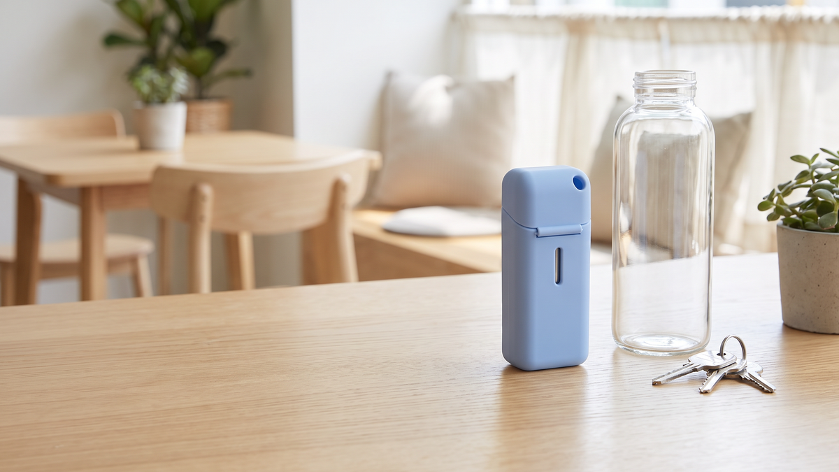 Closed blue straw case on a wooden table next to a glass bottle and keys
