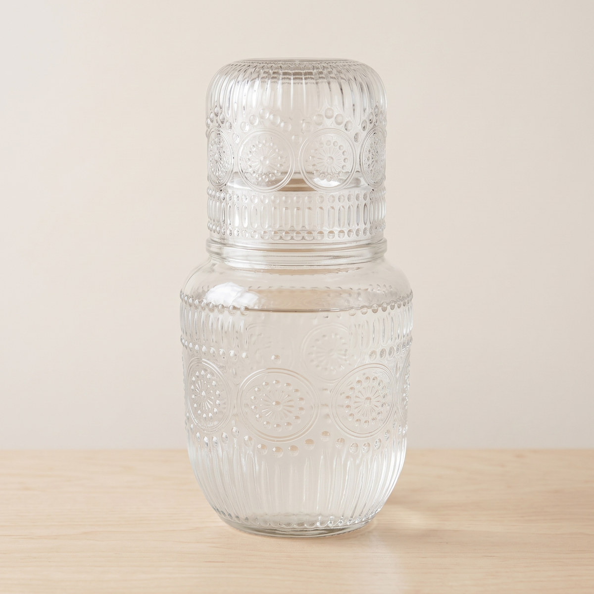 Clear glass carafe filled with water, its glass resting on top, on a pale table