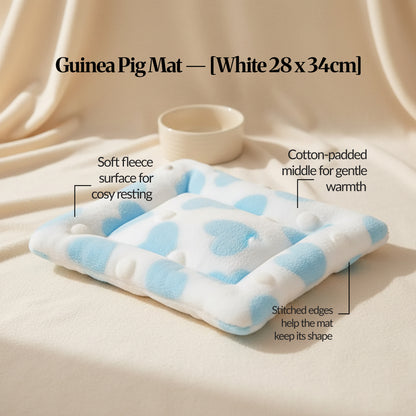 Guinea pig bed mat (White, 28×34cm) on a cream fabric backdrop with a small bowl, highlighting soft fleece, padded centre and stitched edges.