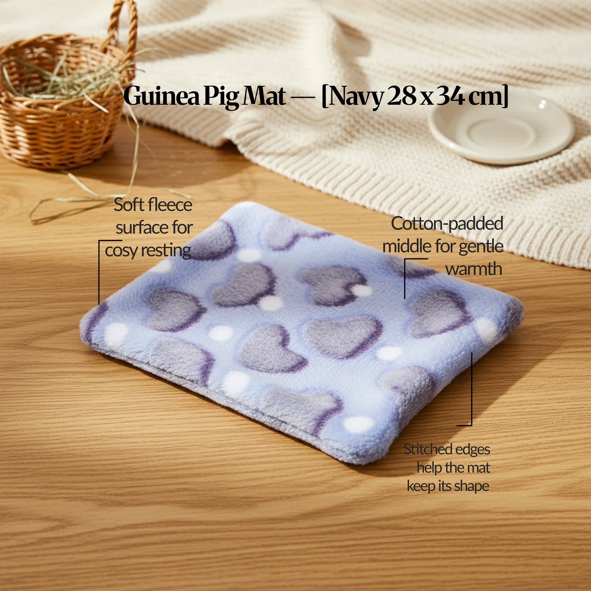 Navy guinea pig bed mat (28×34cm) soft fleece, cotton-padded mat with stitched edges, shown on a wooden table with feature callouts.