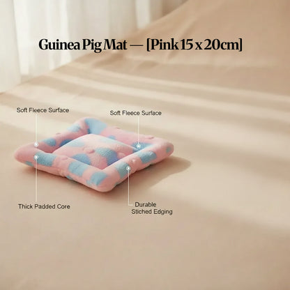 Pink guinea pig bed mat (15×20cm) with soft fleece surface, padded core and stitched edging, shown on a neutral background with feature callouts.