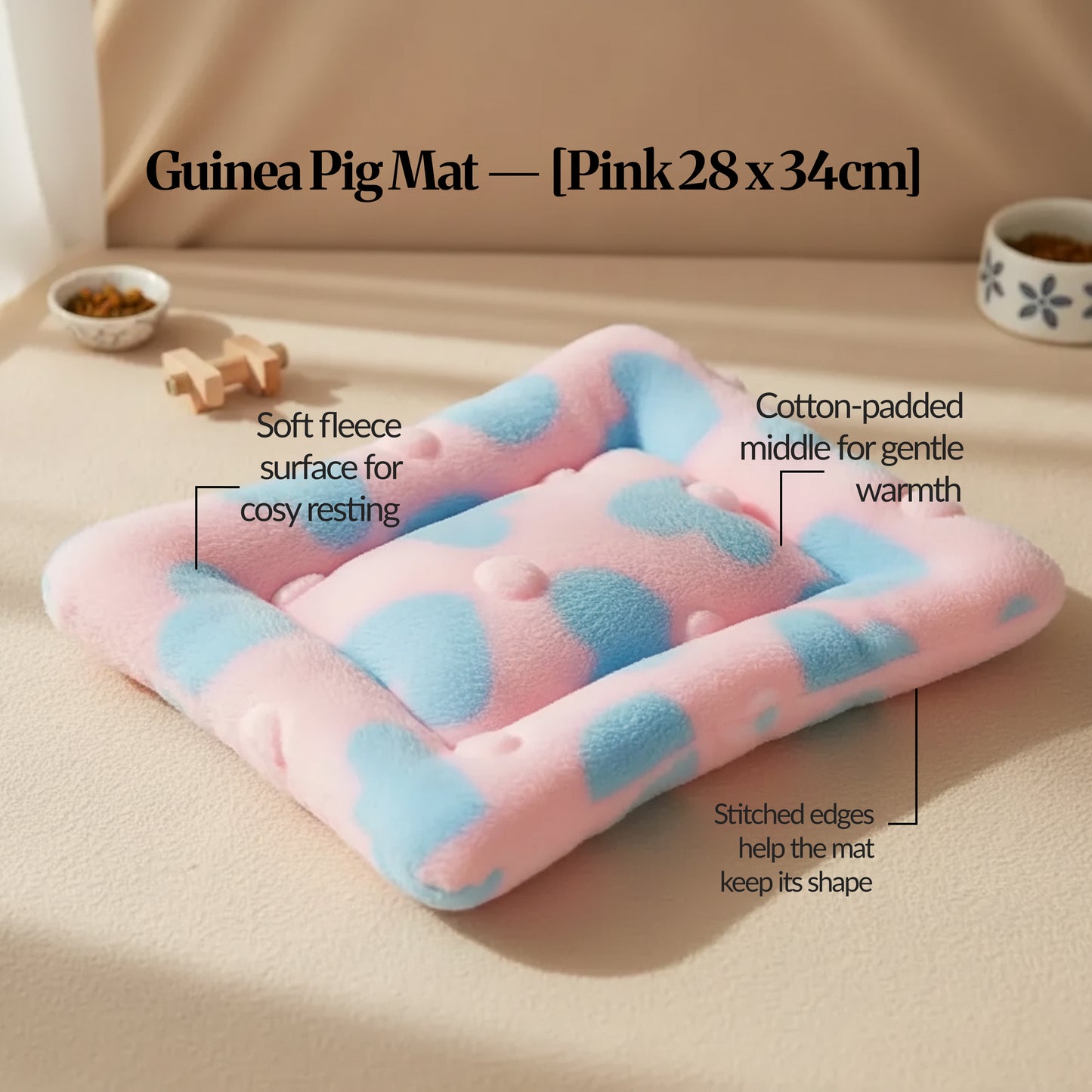 Pink guinea pig bed mat (28 × 34 cm) with soft fleece surface and stitched edges, shown on a light floor with small pet bowls in the background.