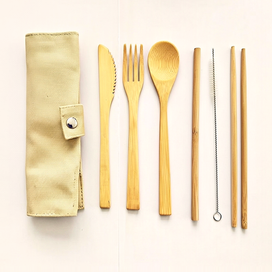 Bamboo travel cutlery laid out in a row beside its rolled cloth pouch: knife, fork, spoon, straw and brush