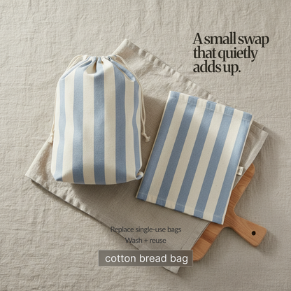 Blue-and-cream striped cotton bread bag and matching liner on linen cloth beside a wooden cutting board; reusable, washable alternative to single-use bags.