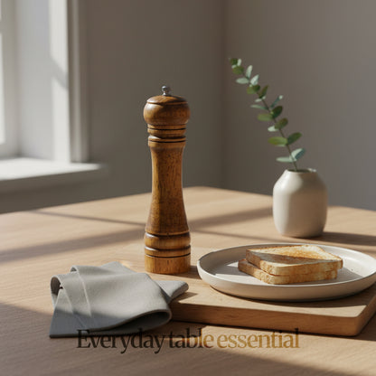 Lifestyle scene of walnut brown wood pepper grinder on wooden table beside plate and toast, soft natural light; “Everyday table essential."