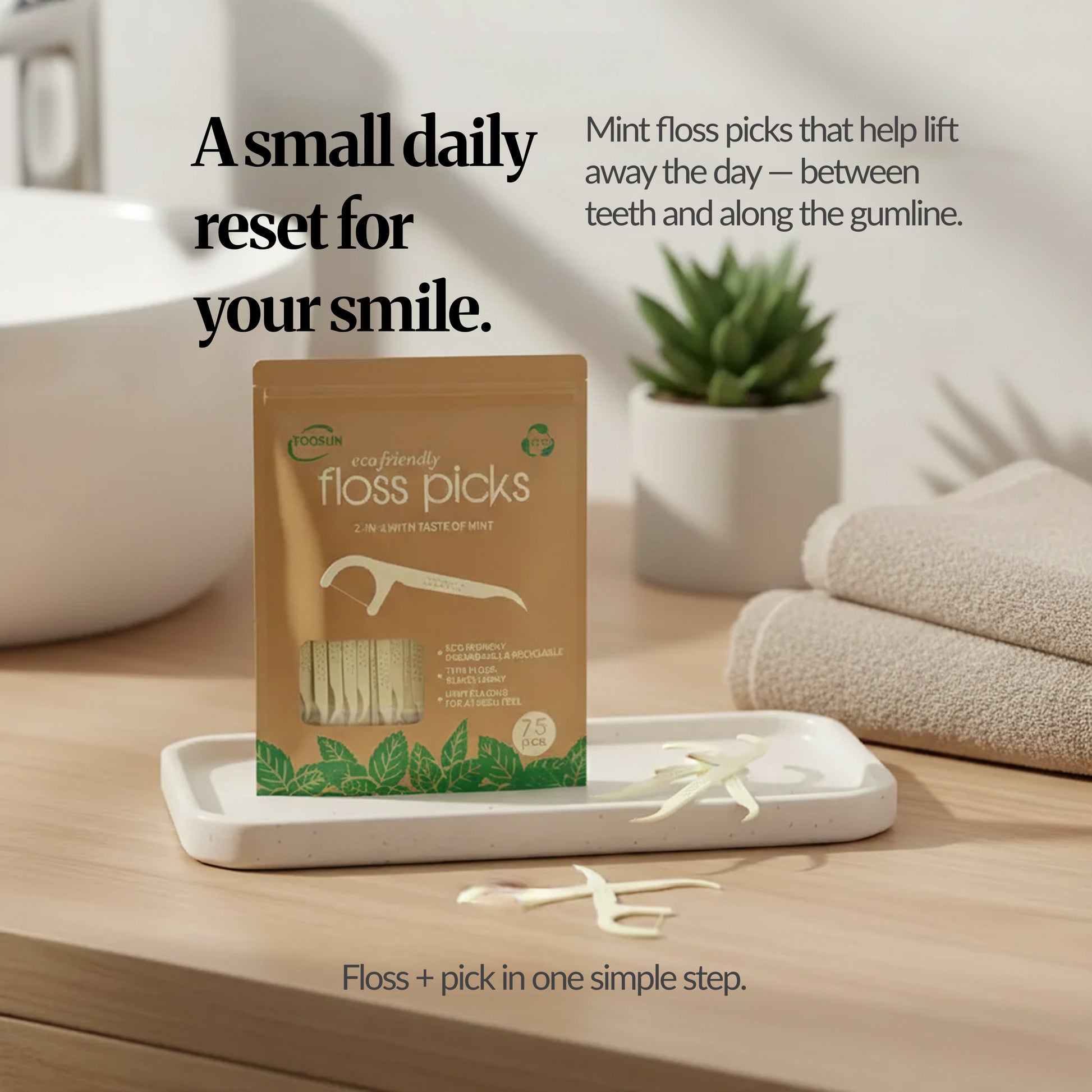 Lifestyle bathroom scene with the floss picks pack on a tray, loose floss picks and folded towels, with text "A small daily reset for your smile."