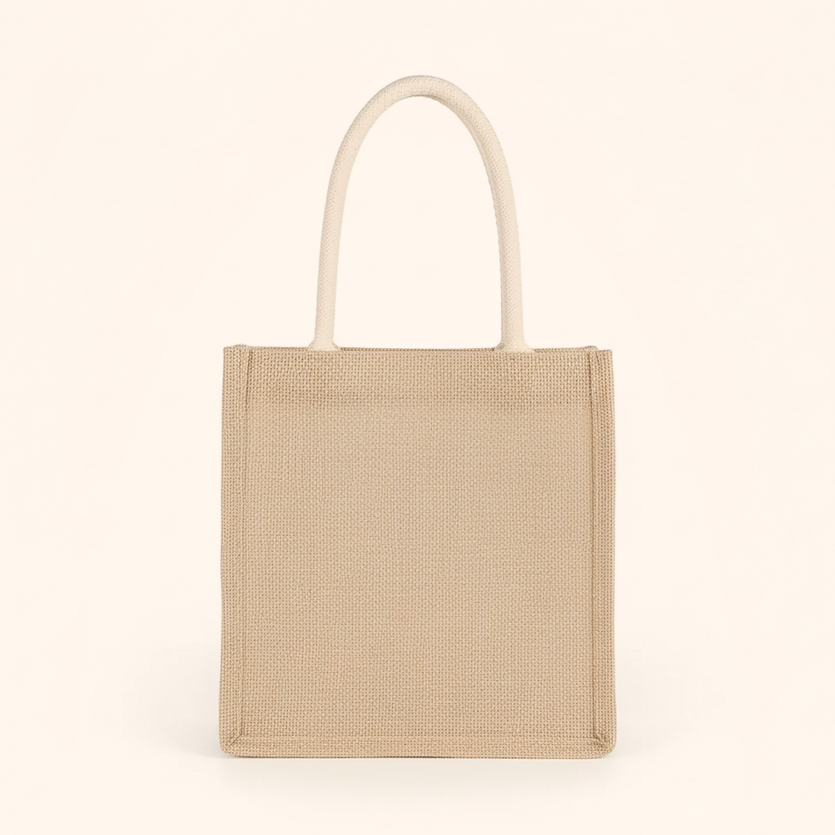 Medium woven tote bag with two cream rope handles, standing upright on cream