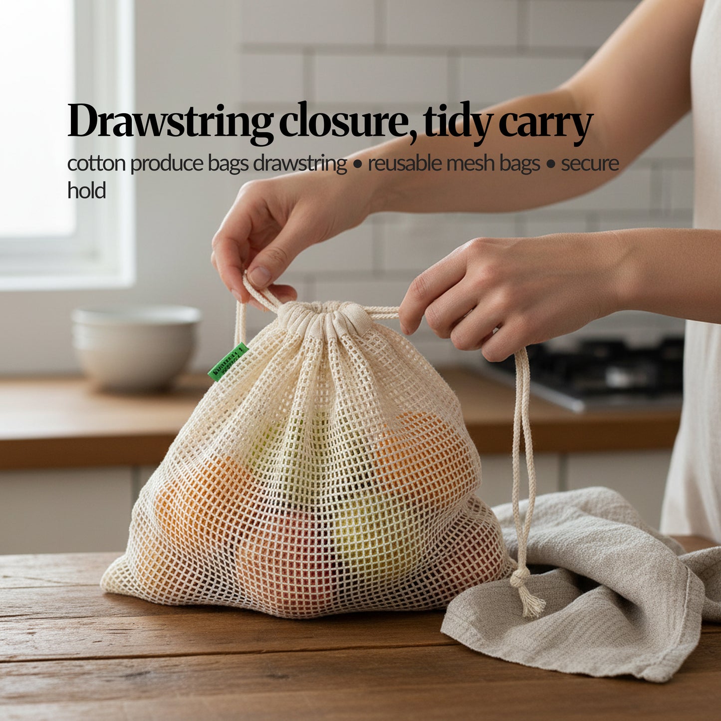 Hands pulling the drawstring closed on a cotton mesh produce bag filled with groceries, demonstrating a secure, tidy carry.