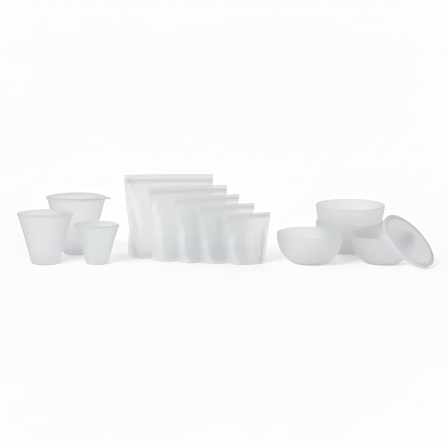 PR069 translucent/clear silicone food storage set laid out on a white background — reusable cups plus zip-top silicone bags and lidded bowls (complete set).