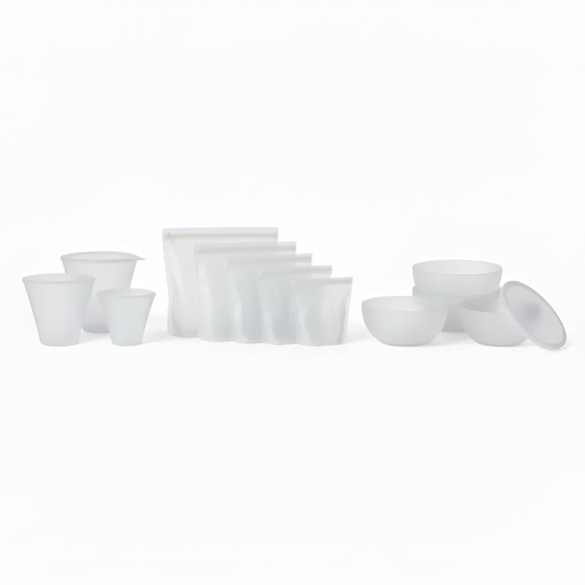 PR069 translucent/clear silicone food storage set laid out on a white background — reusable cups plus zip-top silicone bags and lidded bowls (complete set).