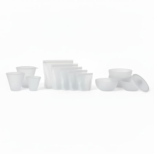PR069 translucent/clear silicone food storage set laid out on a white background — reusable cups plus zip-top silicone bags and lidded bowls (complete set).
