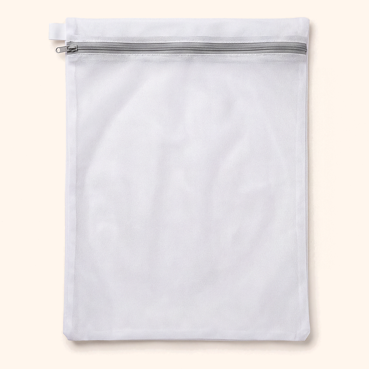 Flat white mesh laundry bag with a grey zip along the top, on cream