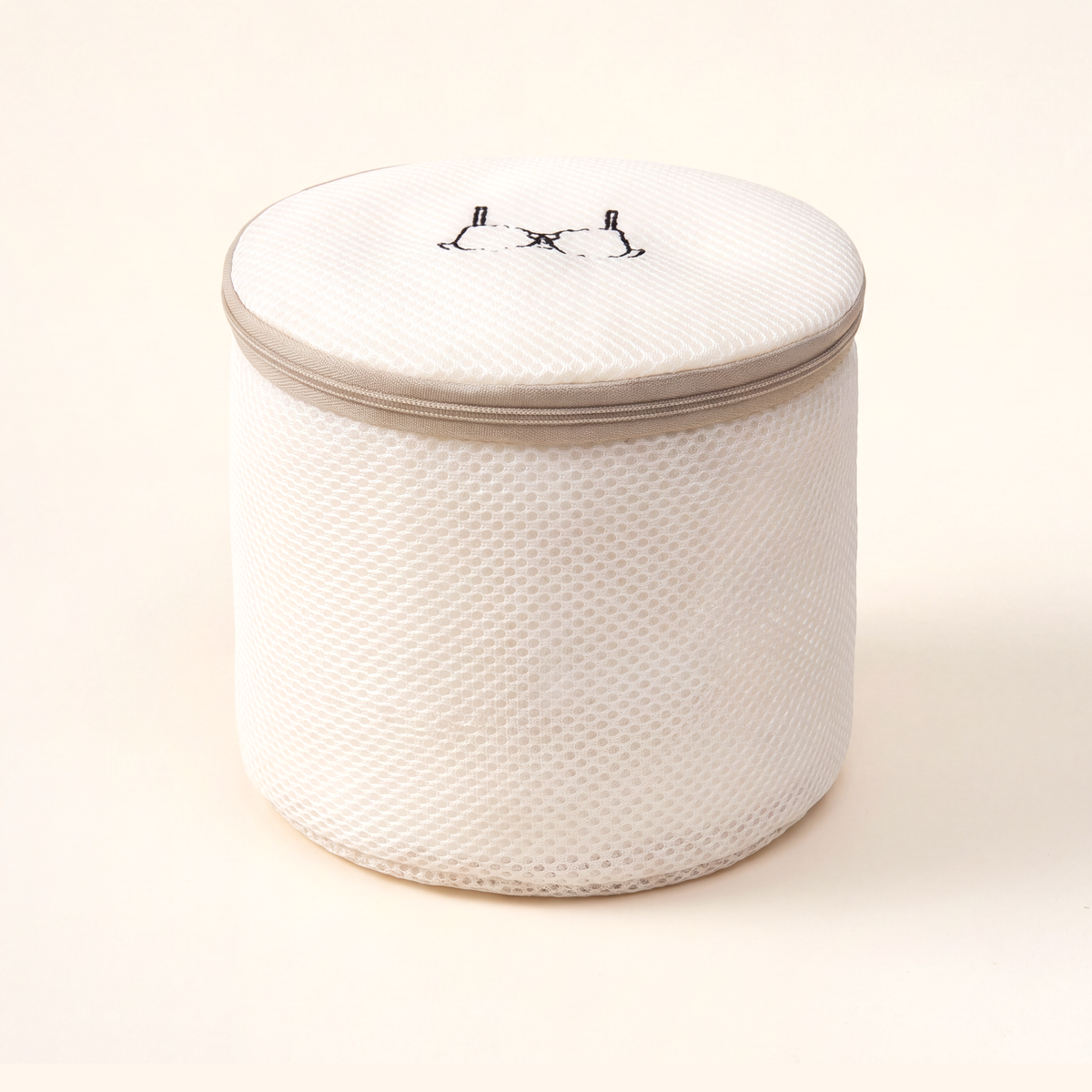 Round cream mesh bra bag with a tan zip around the lid and a bra icon on top