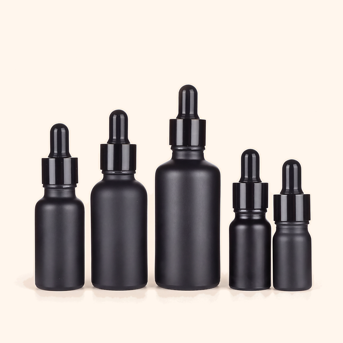 Five matt black glass dropper bottles with black collars in a row, on cream